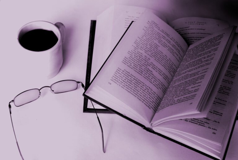 dans des tons violets, photo d'un espace de travail d'une éditrice freelance sur lequel il y a une tasse de café pleine, une paire de lunettes un livre ouvert et un agenda
